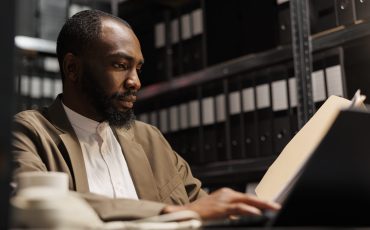 African american prosecutor preparing for case, studying crime matter files in police office. Cop reading forensic expertise report and analyzing investigation clues at night time